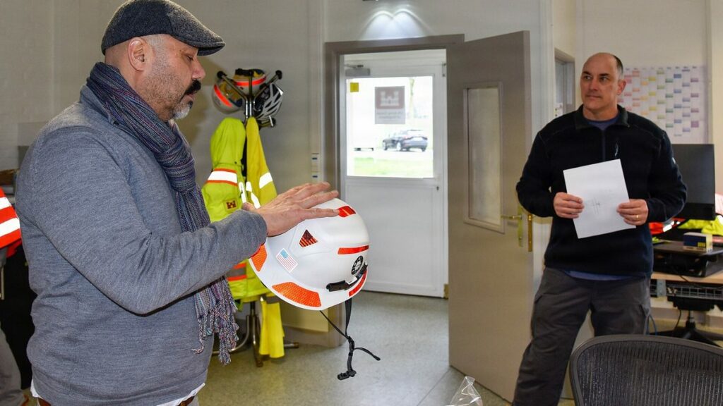 Réunion de prévention des risques dans un atelier, un responsable présente un casque de sécurité à un collègue